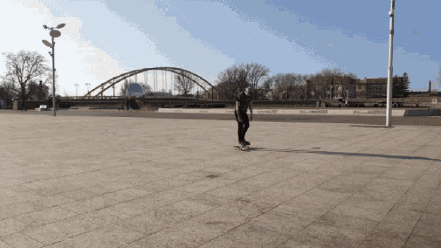 a person riding a skateboard on a sidewalk with a bridge behind them