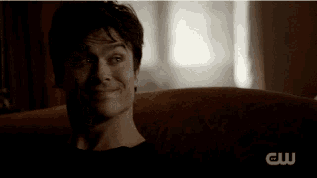 a man is making a funny face while sitting on a couch with a cw logo behind him .