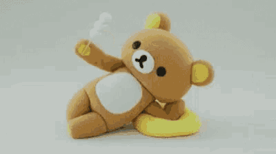 a stuffed teddy bear is laying on a yellow pillow on a white surface .
