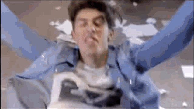 a man in a blue jacket is laying on the floor with his arms outstretched and a picture of superman on his shirt .