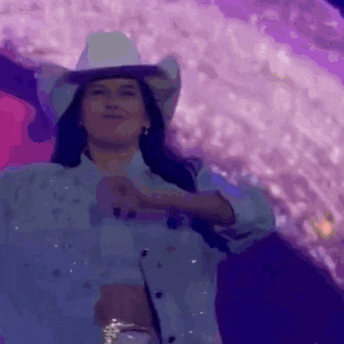 a woman wearing a cowboy hat and a blue shirt is dancing on a stage .