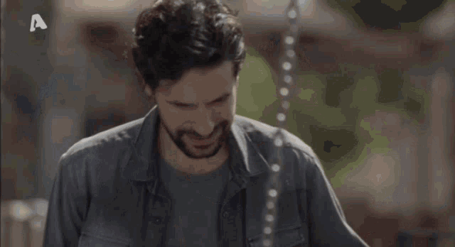 a man with a beard is standing in front of a fence and looking at something .