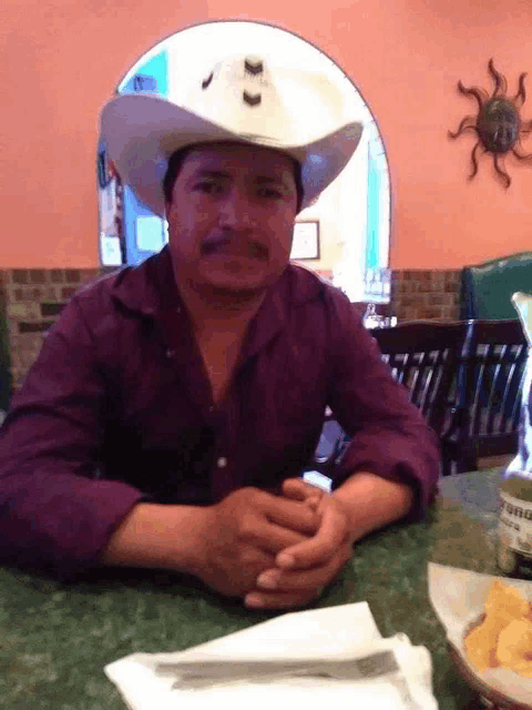 a man wearing a cowboy hat is sitting at a table