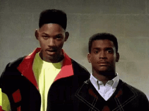 two men are standing next to each other and looking at the camera . one of the men is wearing a yellow shirt .