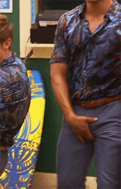 a man in a hawaiian shirt holds his hand to his pants