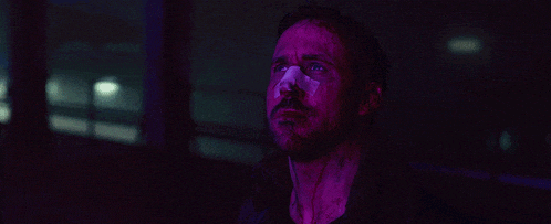 a close up of a man 's face in a dark room with purple lights behind him .