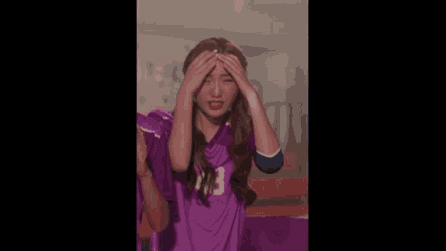 a woman in a purple jersey is covering her face with her hands and making a funny face .
