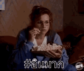 a woman is sitting on a couch eating popcorn and watching a movie .