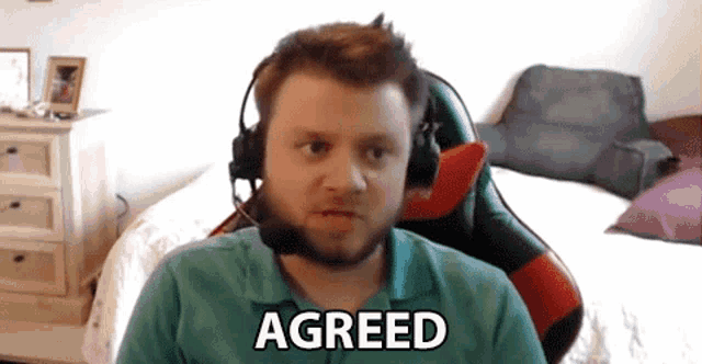 a man wearing headphones and a headset is sitting in a chair and says agreed .