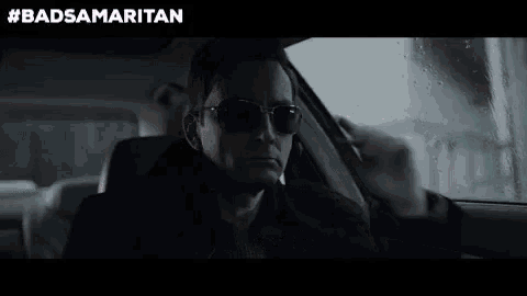 a man is sitting in the driver 's seat of a car wearing sunglasses and smoking a cigarette .