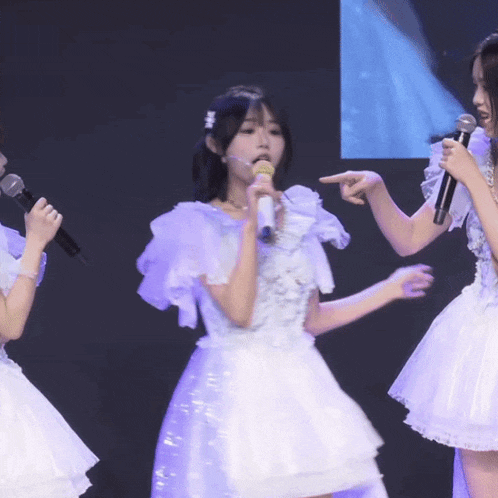 a girl singing into a microphone with another girl pointing