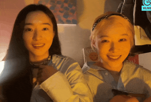 two women are smiling in front of a sign that says vlive on it