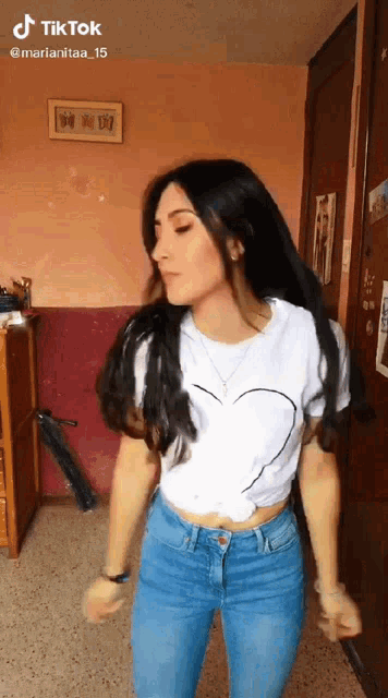 a woman in a white shirt with a heart on it is dancing in a room .