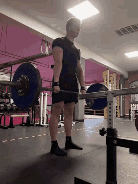 a man lifting a barbell in a gym with a pink wall in the background