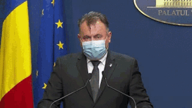 a man in a suit and tie is wearing a face mask and giving a speech .