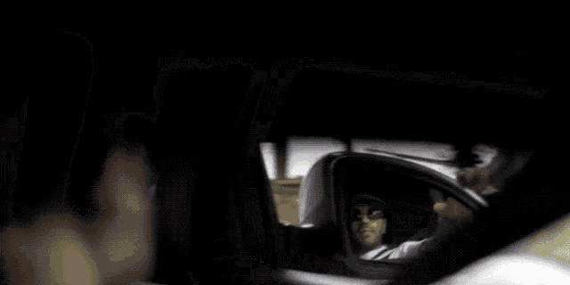 a man driving a car with a reflection of himself in the rear view mirror