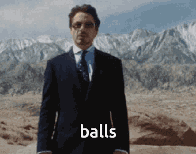 a man in a suit and tie is standing in front of a mountain and the word balls is visible