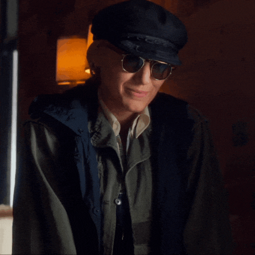 a man wearing a hat and sunglasses is smiling and looking at the camera