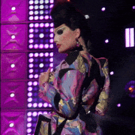 a woman in a colorful dress is standing in front of a wall of purple lights