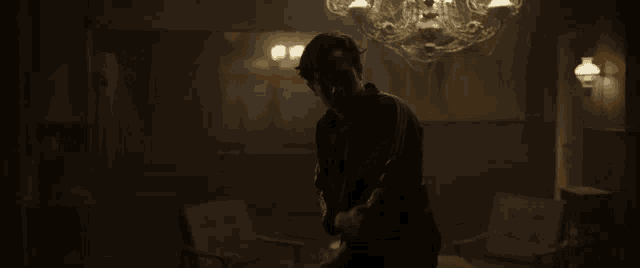 a man is standing in a dark room with a chandelier above him