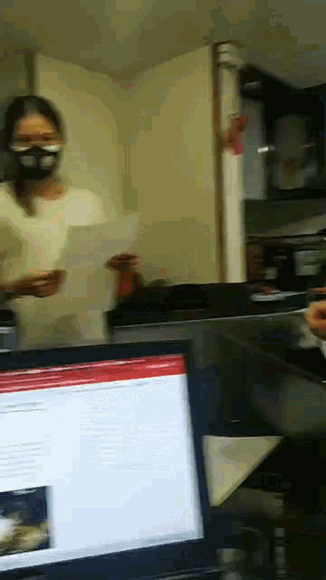 a woman wearing a mask is standing in front of a laptop computer .