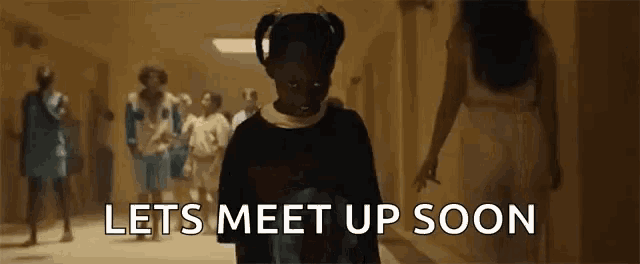 a little girl is standing in a hallway with a group of people walking in the background .