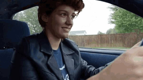 a woman in a leather jacket is sitting in the driver 's seat of a car