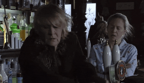 two women at a bar one of whom is holding a card that says ' a ' on it