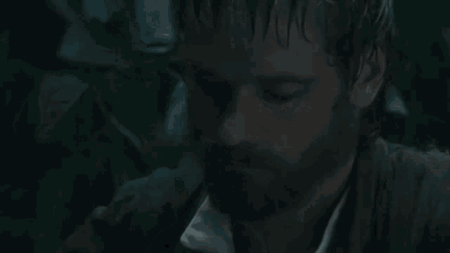 a man with a beard is standing in the dark with his eyes closed .