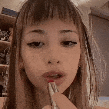 a young woman is applying red lipstick to her lips .