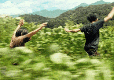 a man and woman are running through a field with their arms in the air