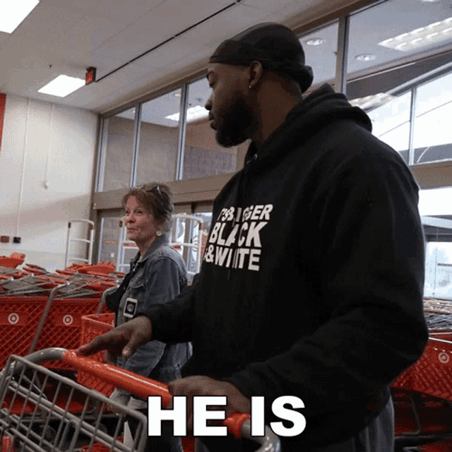 a man wearing a black shirt that says black and white pushes a shopping cart