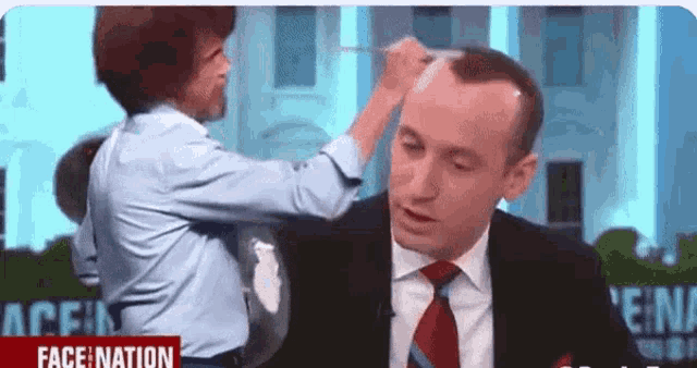 a man in a suit and tie is getting his hair done by a woman in a blue shirt .