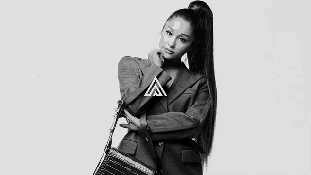 ariana grande is wearing a blazer and a ponytail and holding a purse .