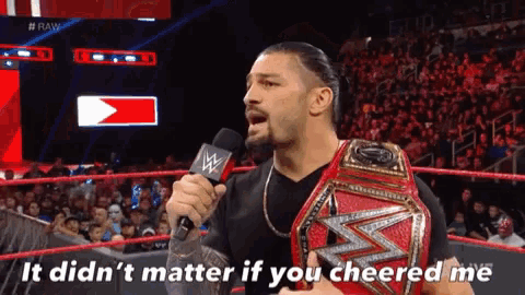 roman reigns is talking into a microphone while holding a wrestling championship belt