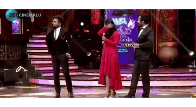 a woman in a red dress is being held by two men on a stage with a sign that says zee cine alu