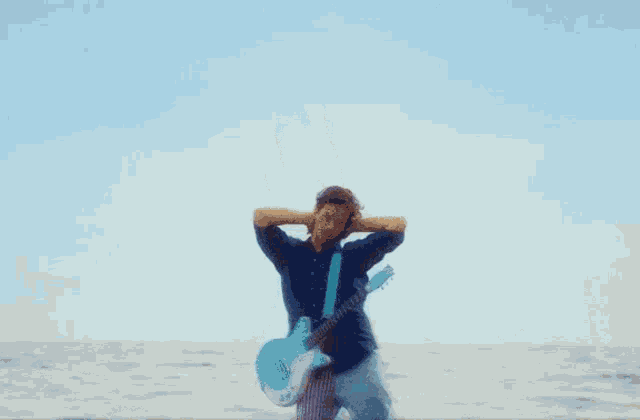 a man in a blue shirt is holding a blue guitar in front of the ocean