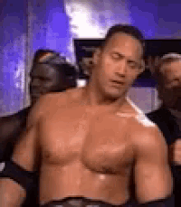 a shirtless wrestler is standing in front of a group of people .
