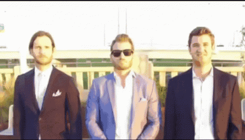 three men in suits and sunglasses are standing next to each other on a balcony