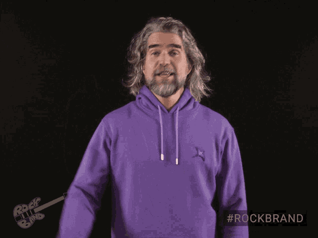 a man wearing a purple hoodie with a rock band logo behind him