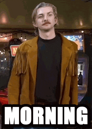 a man with a mustache is wearing a brown jacket and standing in front of an arcade machine that says morning .