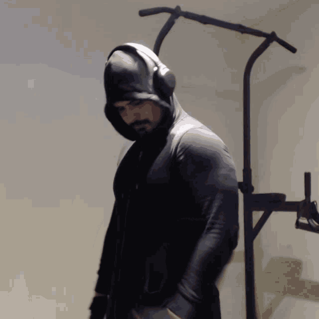 a man wearing a hoodie and headphones stands in front of a gym equipment
