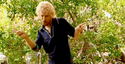 a man with curly blonde hair is standing in front of a blender in the woods .
