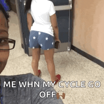 a woman in shorts is standing next to a man in a hallway and says `` me when my cycle go off ''
