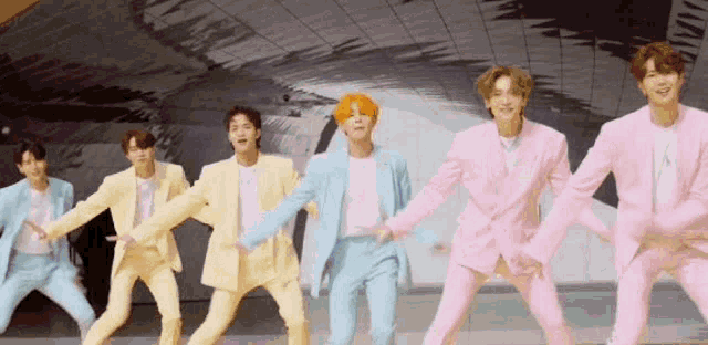 a group of men in pink and yellow suits are dancing in a line .