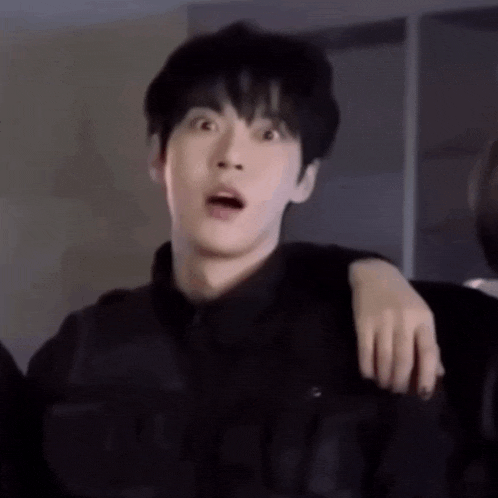 a young man is making a surprised face while standing next to another young man .