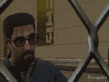 a man with glasses and a beard is behind a metal fence with the name komegatze written on it