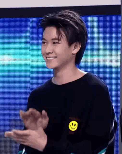 a young man wearing a black sweater with a smiley face on it is clapping .