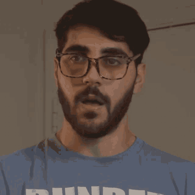 a man with a beard wearing glasses and a blue shirt that says hundred