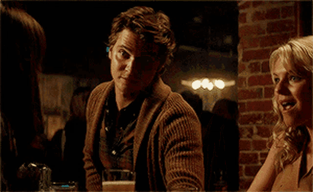 a man in a brown sweater is talking to a woman in a dark room